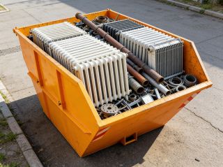 Schrottcontainer auf Einfahrt gefüllt mit alten Heizkörpern und Metallrohren